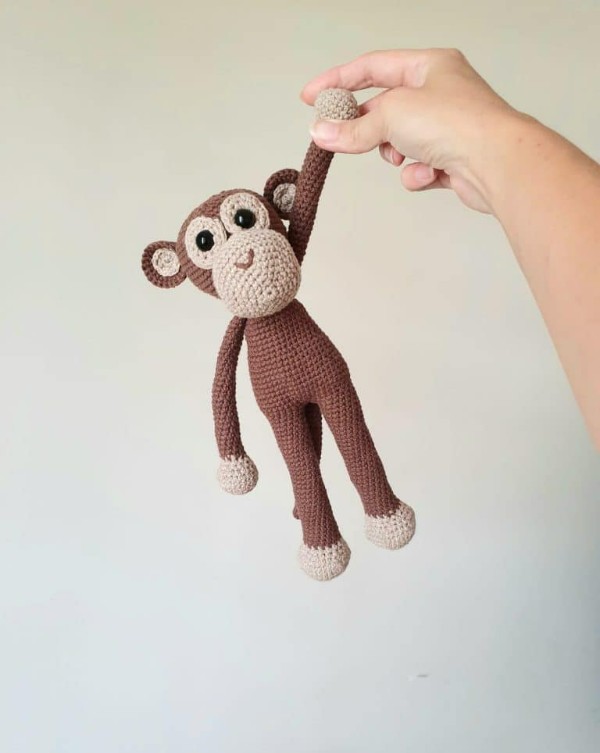 A cheeky crochet monkey being held by one hand.