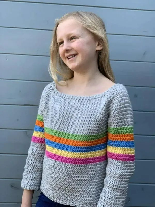 A child wearing a raglan-style crochet sweater with rainbow stripes.