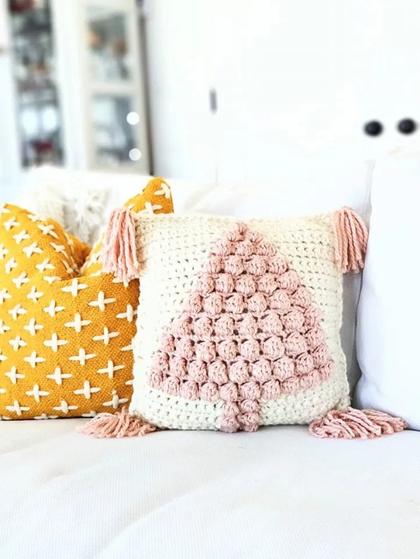 A crochet pillow with pink tassels and a puff stitch tree motif.