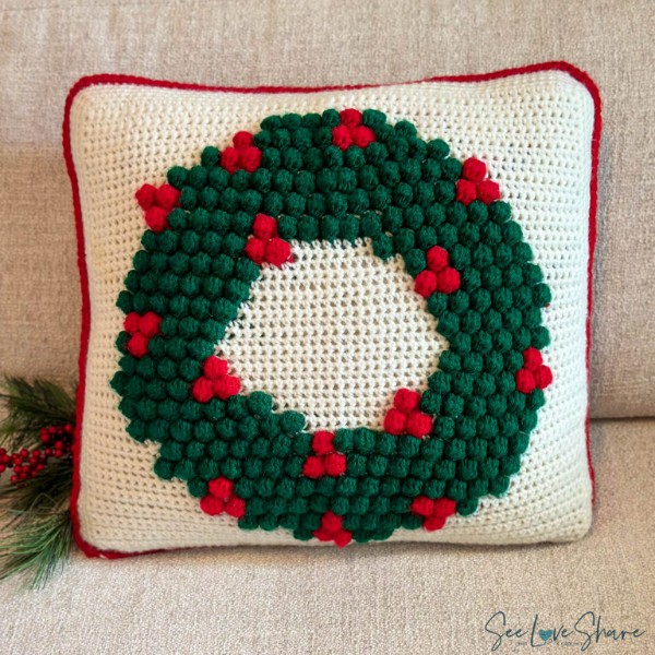 A crochet pillow with a christmas wreath pillow.