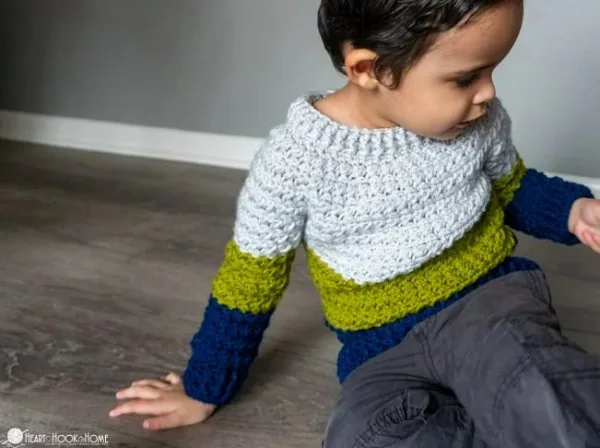 A toddler boy wearing a colour blocked crochet sweater.