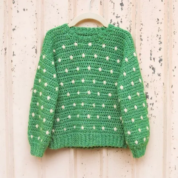 A green crochet kids sweater with white dots.