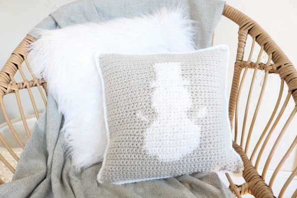 A light gey and white crochet pillow with a tapestry crochet snowman motif.