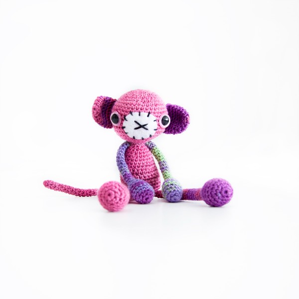 A long-legged amigurumi monkey toy made in bright pink yarn.