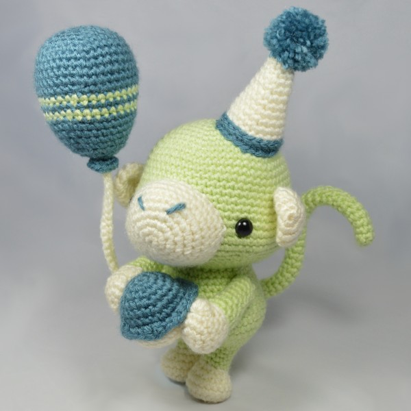 A green crochet monkey holding a balloon.