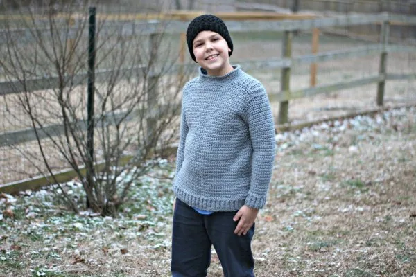 A boy wearing a grey crochet sweater with ribbed shoulder detail.