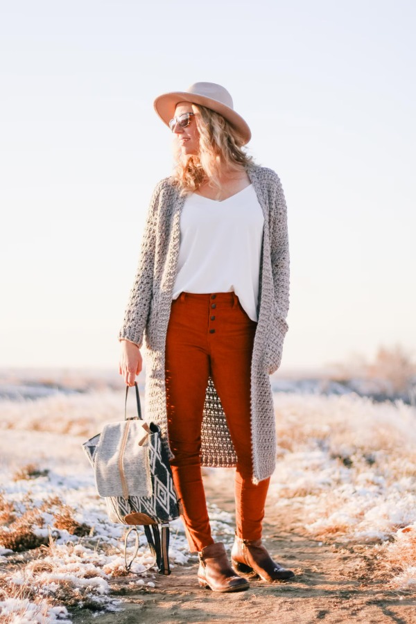  A woman wearing a long grey crochet suster-style cardigan.