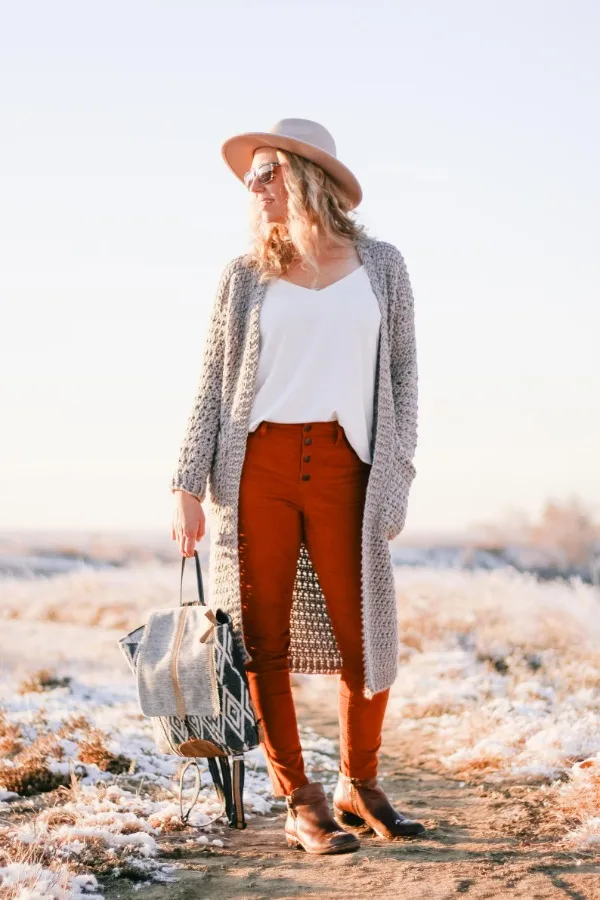  A woman wearing a long grey crochet suster-style cardigan.