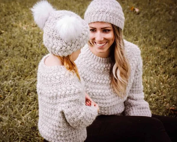 A mother and child wearing matching crochet sweaters and hats.