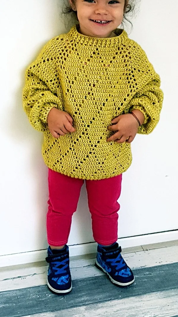 A child wearing a lime green crochet sweater with filet diamond motifs.