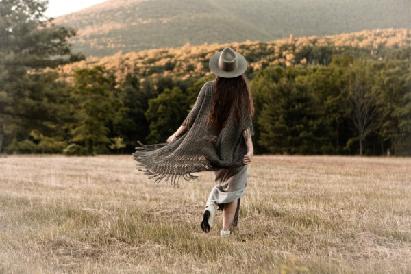 Back view of a woman outdoors wearing a hat and a long crochet duster.