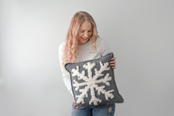 A grey crochet pillow iwth a faux-fur snowflake motif.