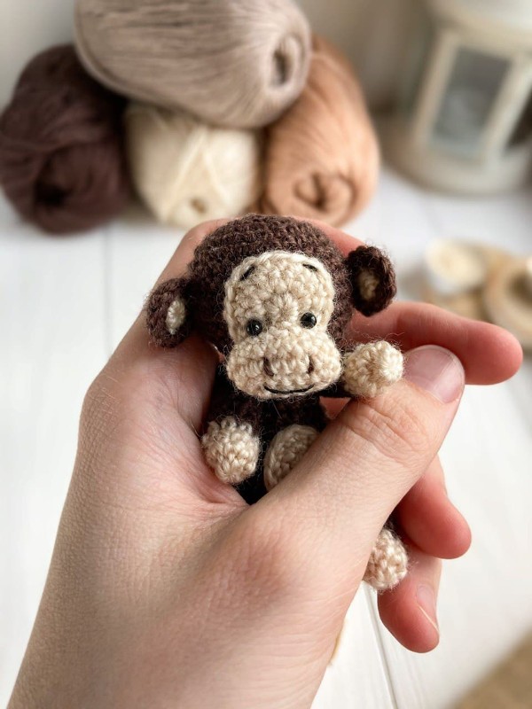 A closeup of a hand holding a tiny crochet monkey toy.