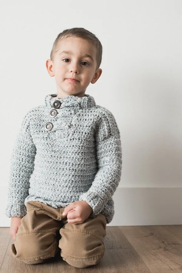 A toddler wearing a grey crochet sweater with buttons.