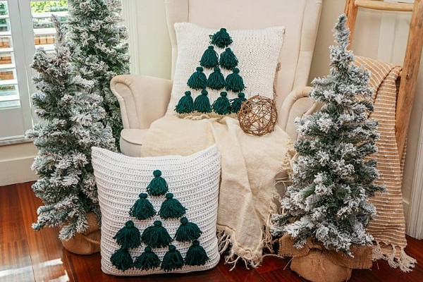 A crochet Christmas pillow with a Christmas tree motif made from green yarn tassels.