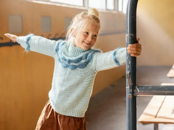 A young girl wearing a pale blue crochet sweater with blue wave pattern details.