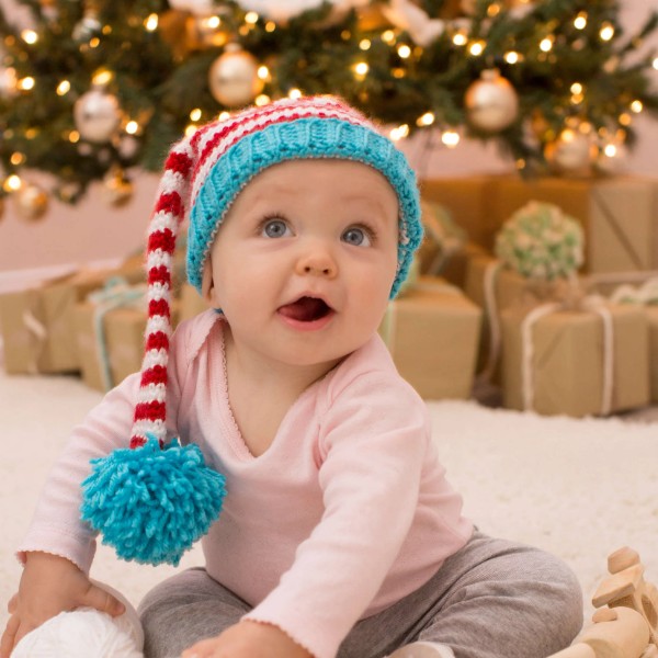 A baby wearing a red, white, and blue crochet elf hat.