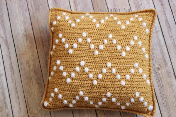 A yellow and white crochet pillow with a bobble-stitch chevron design.