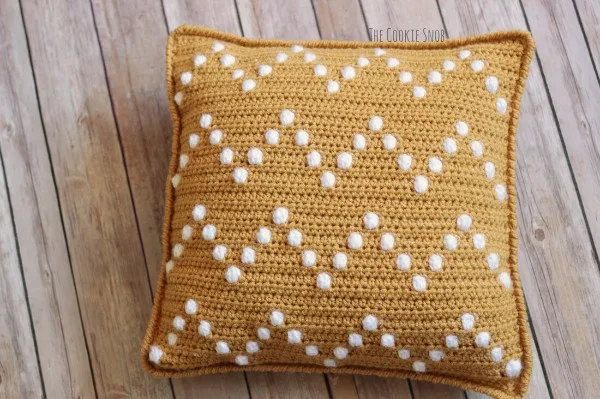 A yellow and white crochet pillow with a bobble-stitch chevron design.