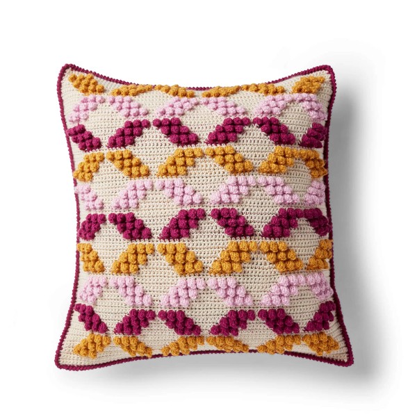 A pink and yellow geometric pattered crochet cushion.