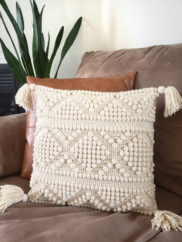 A crem-coloured bobble stitch cushion with corner tassels.