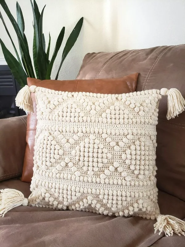 A crem-coloured bobble stitch cushion with corner tassels.