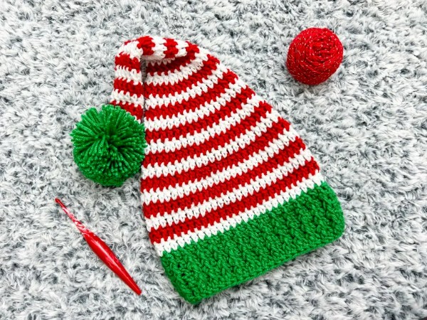 A red and white striped elf hat with a green brim and pompom.