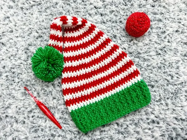 A red and white striped elf hat with a green brim and pompom.