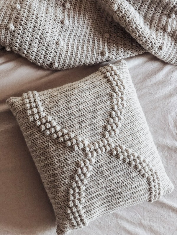 An oatmeal coloured bobble stitch pillow with a simple helix-shaped design.