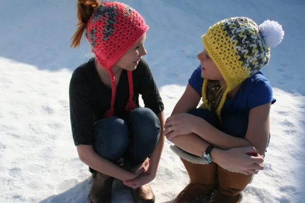 Children wearing crochet beanies with ear flaps and ties.