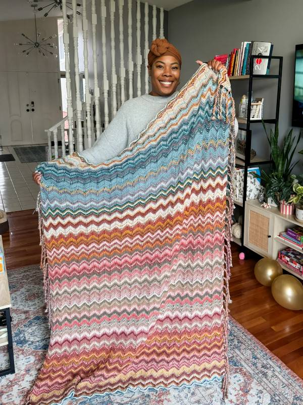 A woman holding up a Tunisian crochet temperature blanket.