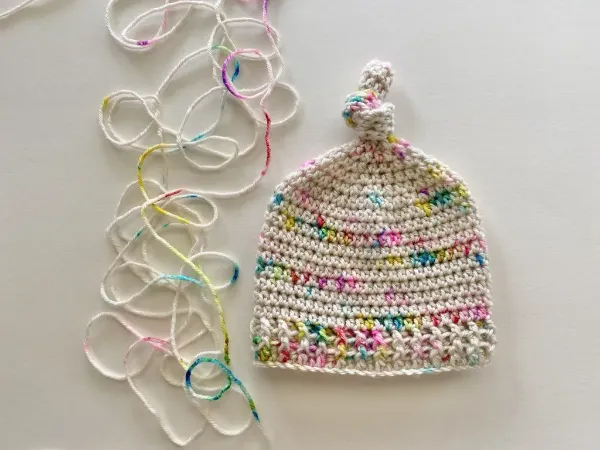 A crochet baby beanie with a tied top knot.