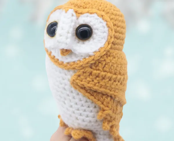A tan and white crochet barn owl amigurumi.