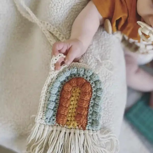 A rainbow-shaped children's crochet bag in modern, muted colours.