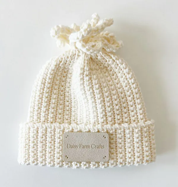 Cream baby beanie with crocheted tassel top.