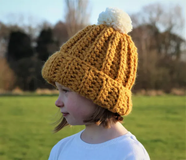 A young child wearig a yellow rib stitch crochet beanie.