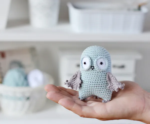 A small crochet owl resting in the palm of a hand.