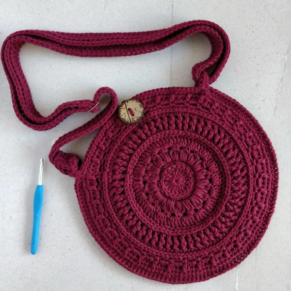 A burgundy coloured crochet circle bag with button closure.