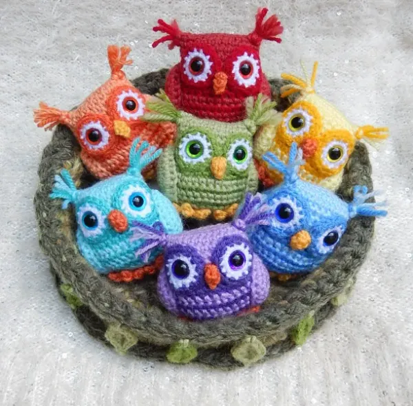 A crocheted nest filled with miniature amigurumi owls in rainbow colours.