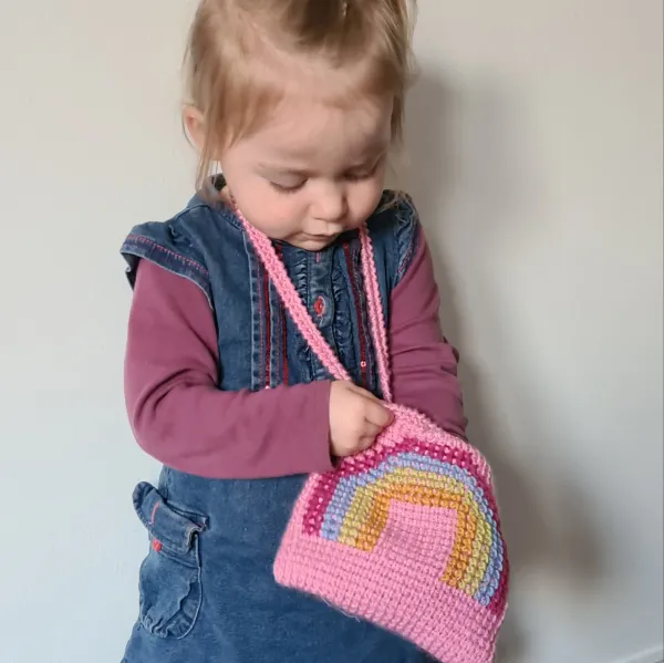 A young child with a rainbow crochet bag.