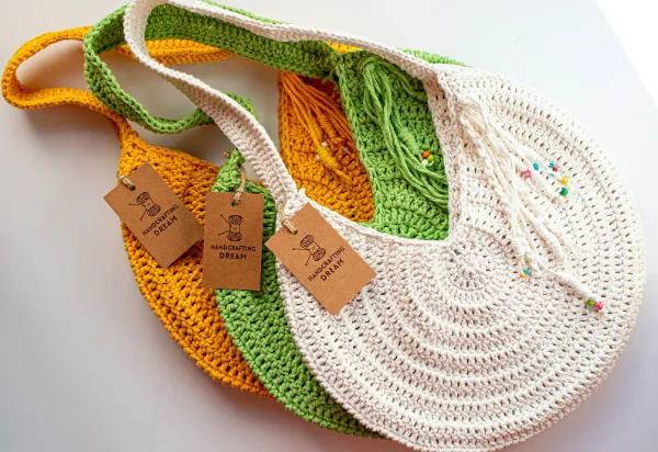 Three round crochet tote bags in white, orange, and lime green.