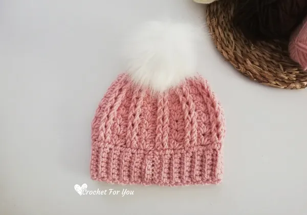 A pink childs beanie with a faux fur pompom.