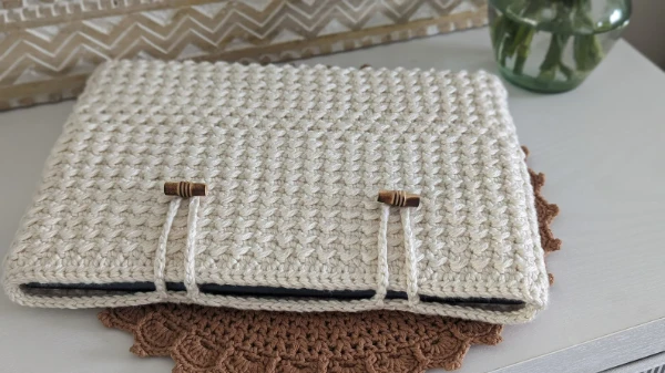 A cream-coloured, textured crochet laptop sleeve with wooden toggle closures.
