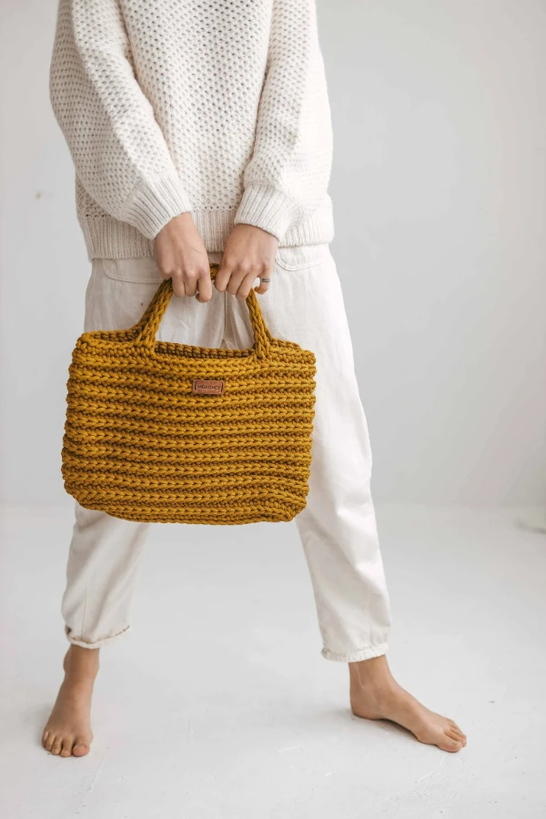 A woman in casual clothes carrying a mustard yellow crochet laptop bag.