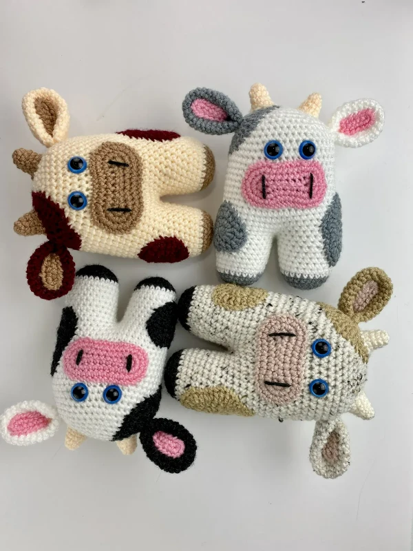 Four crochet cow toys in different colours.