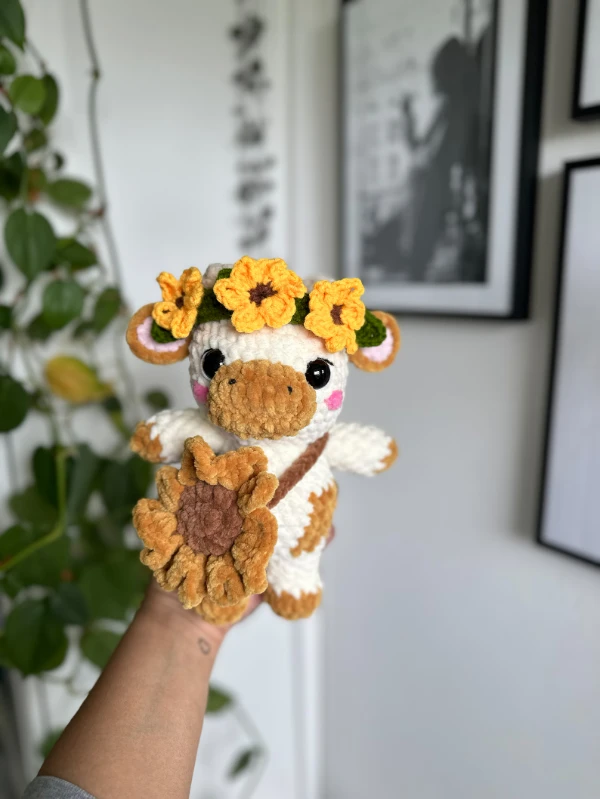 A crochet cow with a sunflower crown and bag.