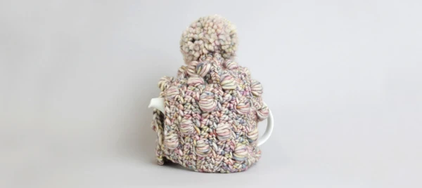 A teapot with a chunky crochet cosy.
