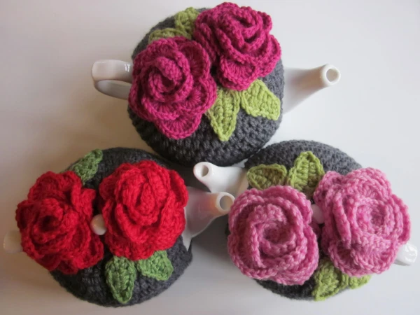 Three crochet teapot covers decorated with crochet roses.