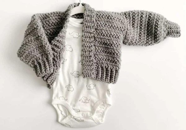 Flat lay image of grey bomber-style newborn baby cardigan and a white onesie.
