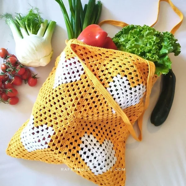 A crochet market bag eaturing heart motifs filled with vegtables.